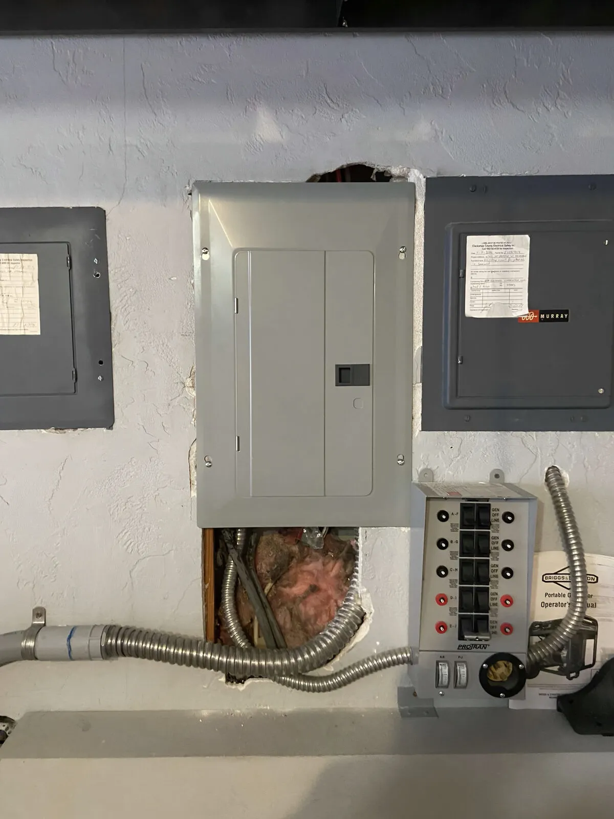 Drywall damage around electrical panel with exposed insulation and tubing before repair