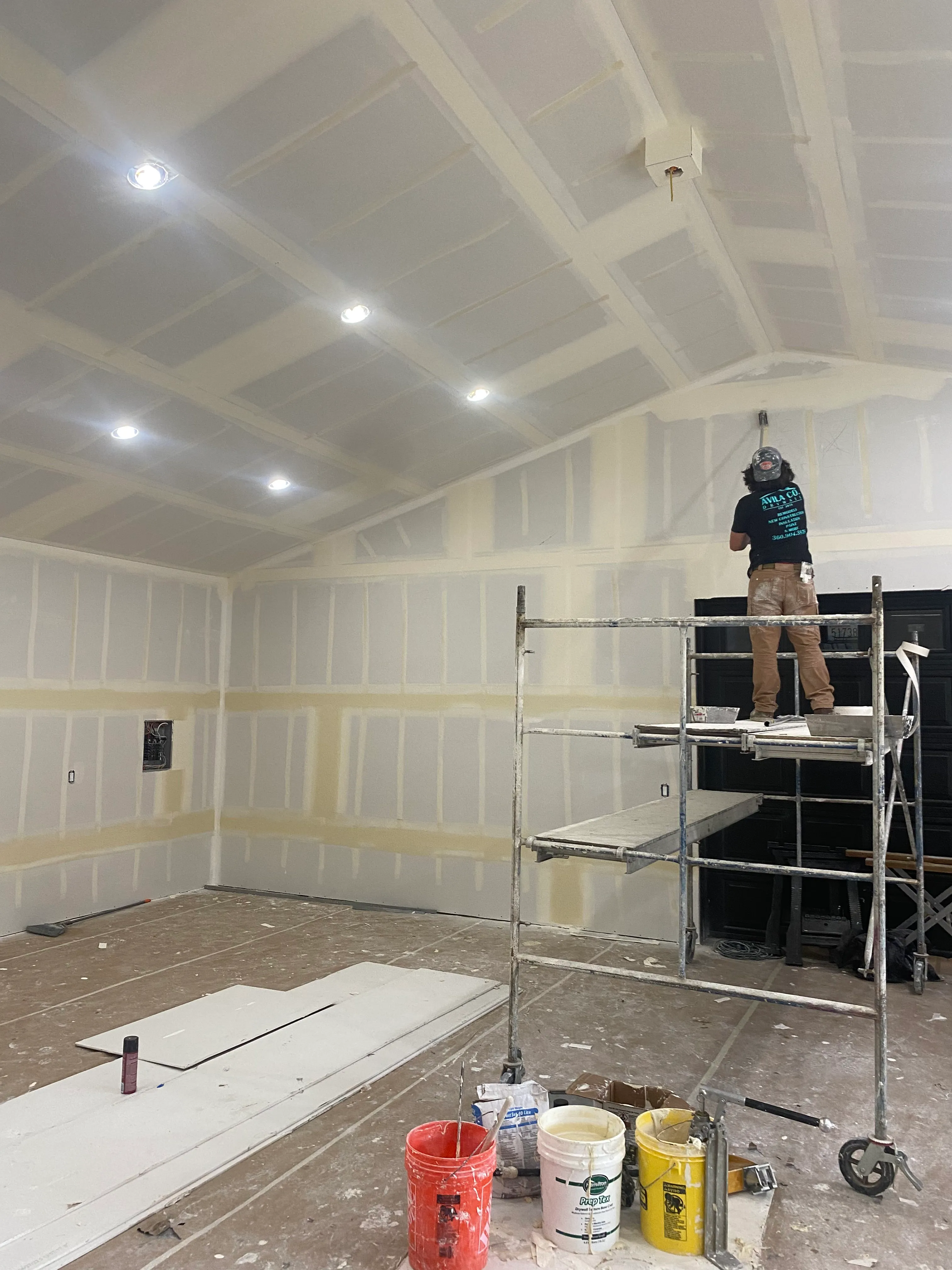 AvilaCo Drywall crew member taping drywall seams on scaffolding in garage conversion