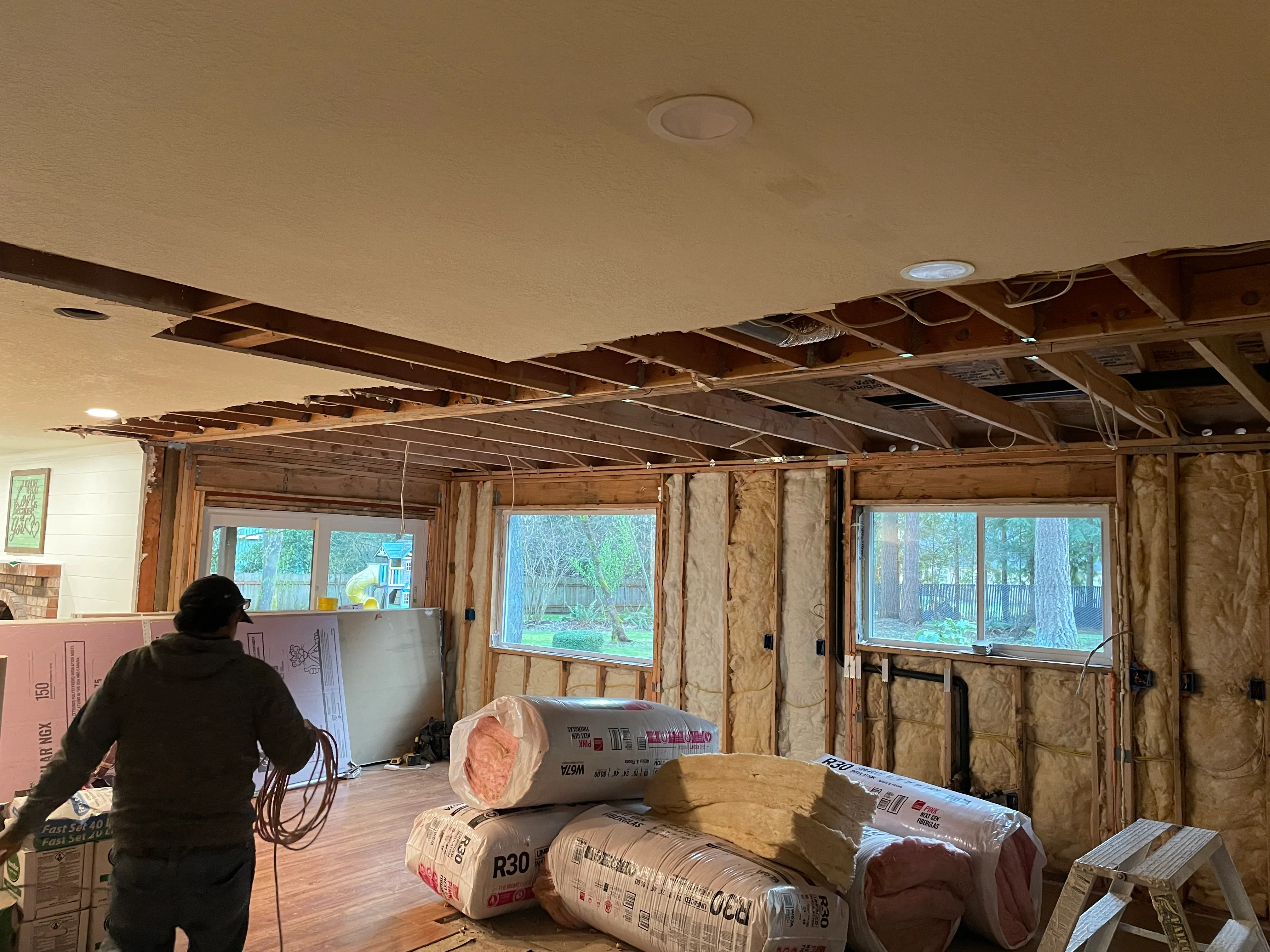 Crew member with batt insulation rolls in room with open ceiling framing during insulation installation