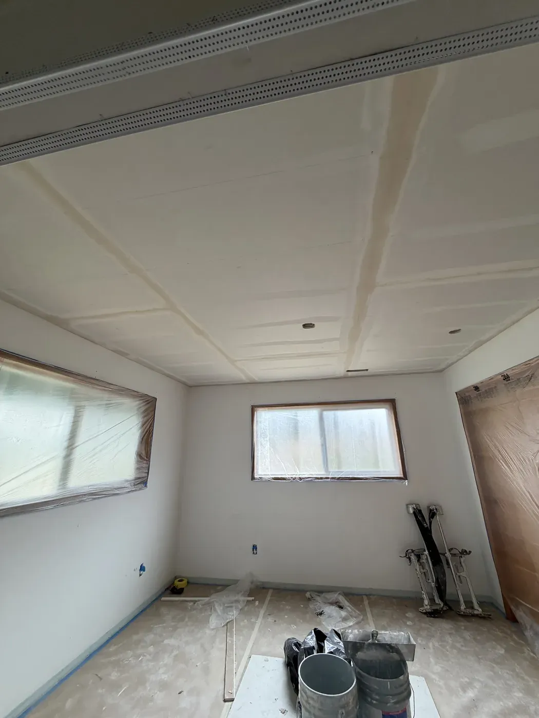 Taped drywall ceiling joints and light openings above masked windows during a Vancouver ceiling overlay