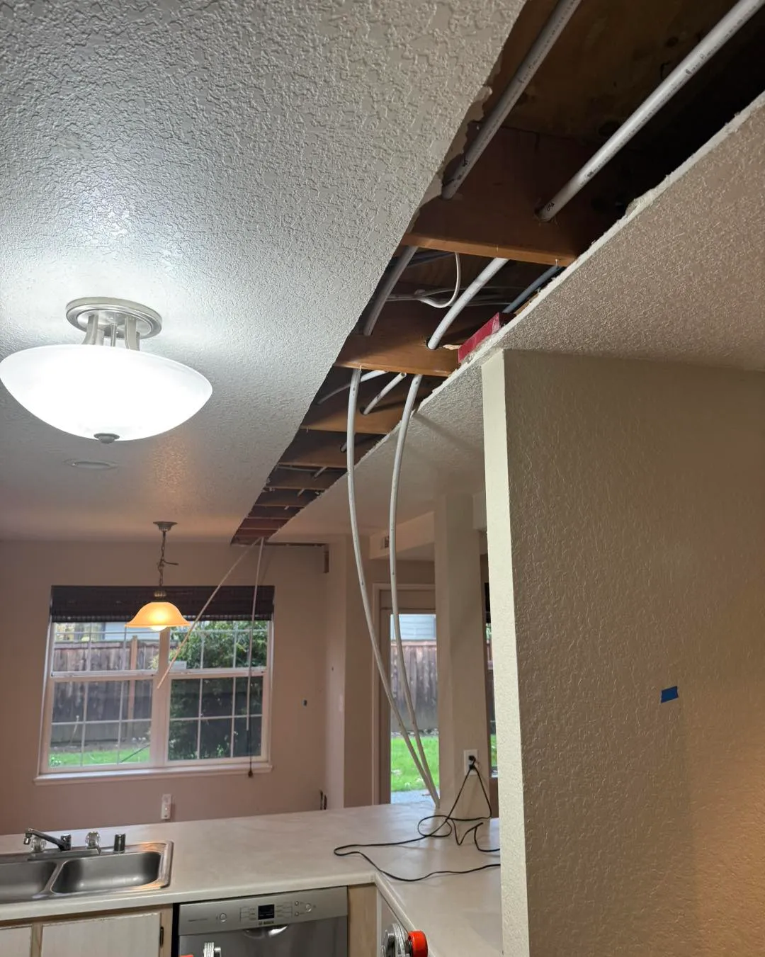 Kitchen ceiling torn open exposing joists and new PEX piping after whole-home repipe