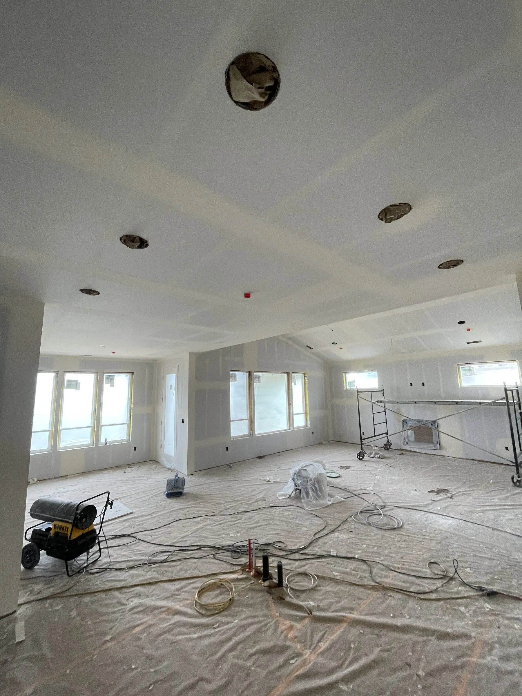 Large open room with drywall hung and taped on the walls and ceiling, boxed soffits overhead and scaffolding on the floor