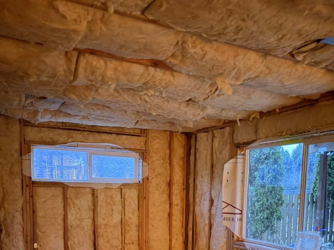 Small room insulated on every wall and across the ceiling before drywall, with two windows framed in
