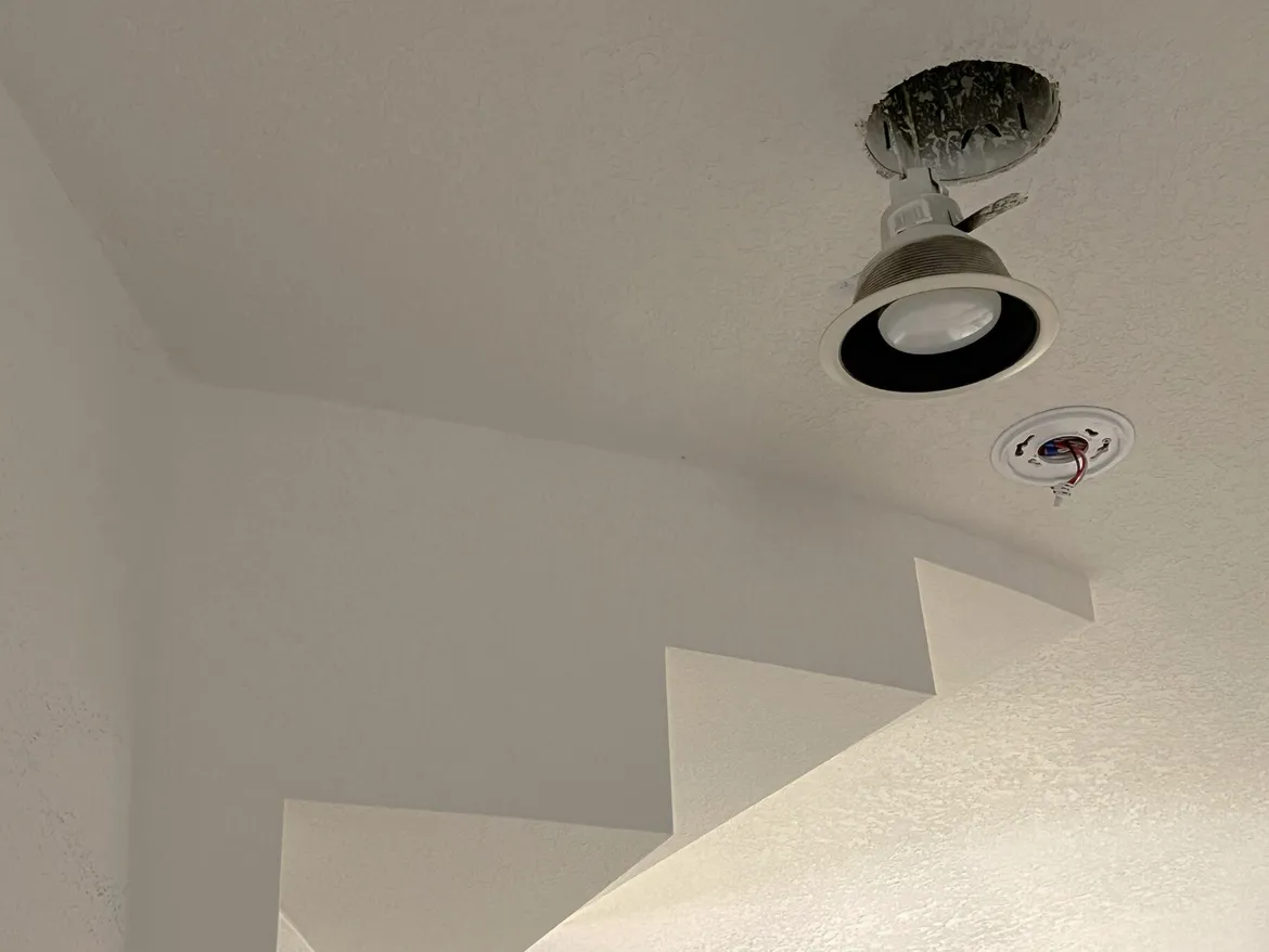 Stairwell with smooth painted drywall walls, the zigzag edge of the stair stringer in drywall and a recessed light can being installed