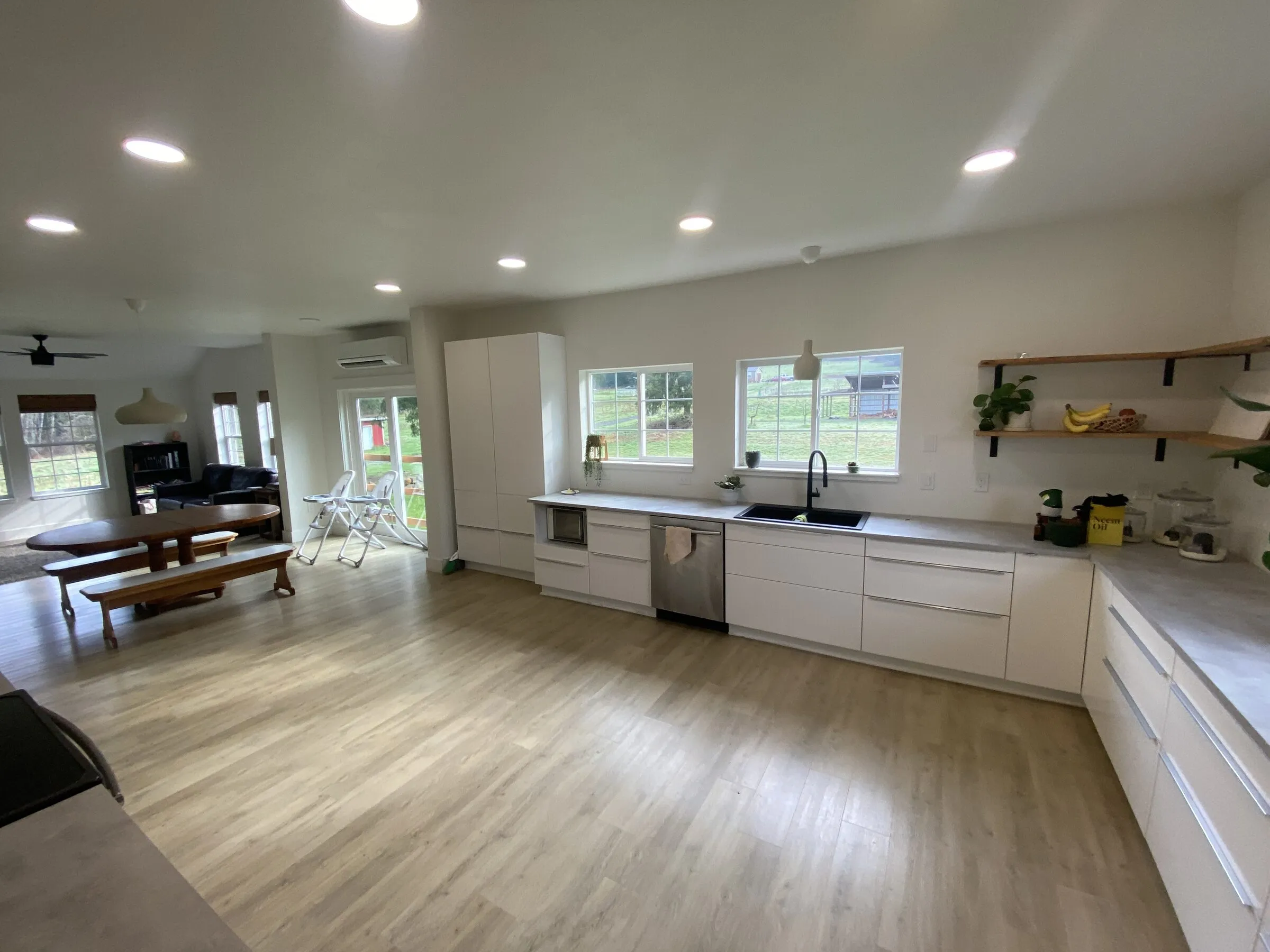 Bright finished open kitchen and great room with smooth white walls and ceiling, recessed lights, white cabinets and a dining table