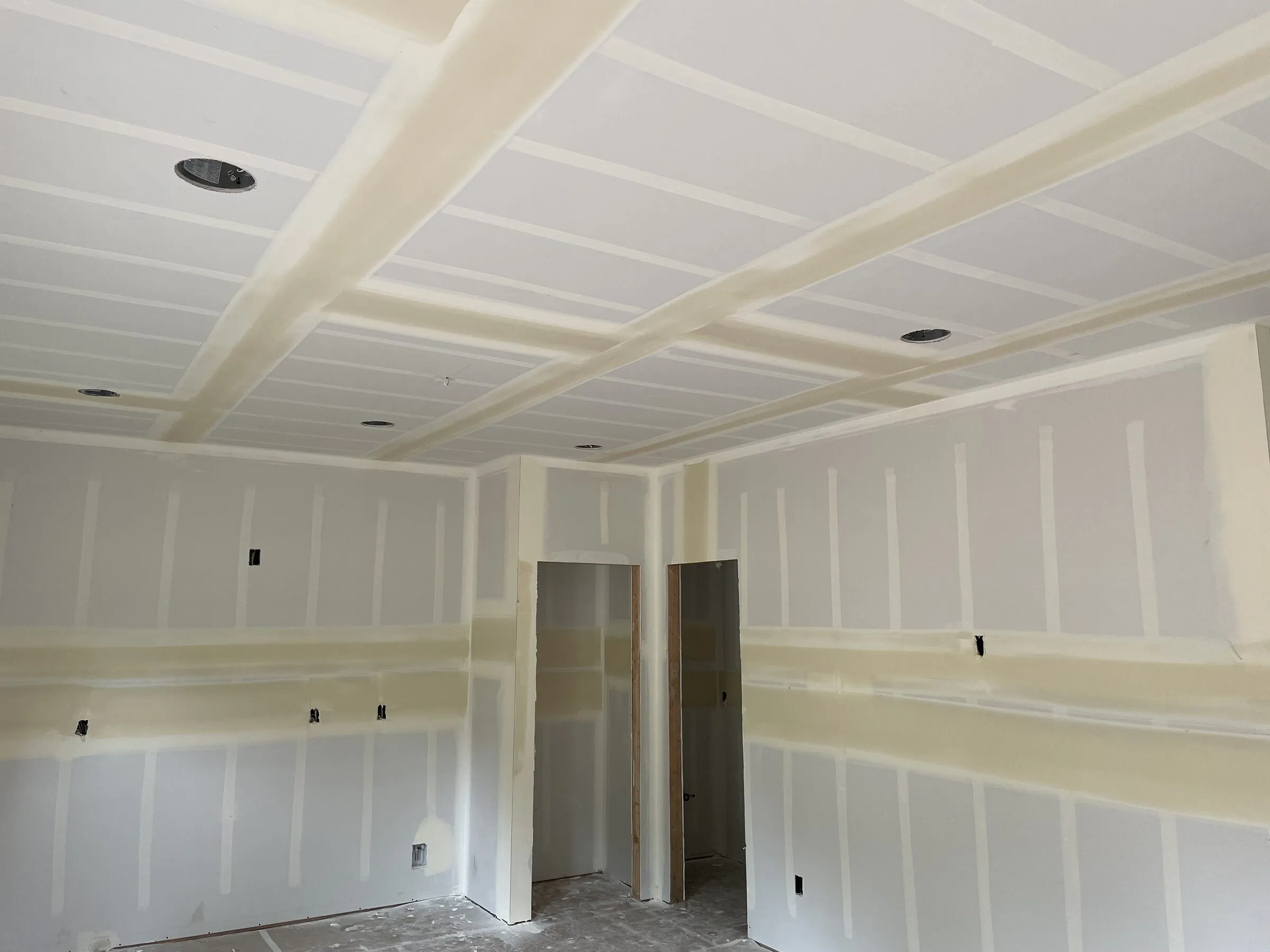 Ceiling with boxed soffits running across it in a grid, taped and mudded, with recessed light cans and two closet openings