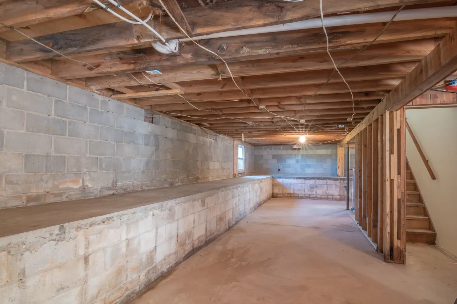 Unfinished basement with concrete block walls, exposed floor joists, and a framed wall opening beside the stairs