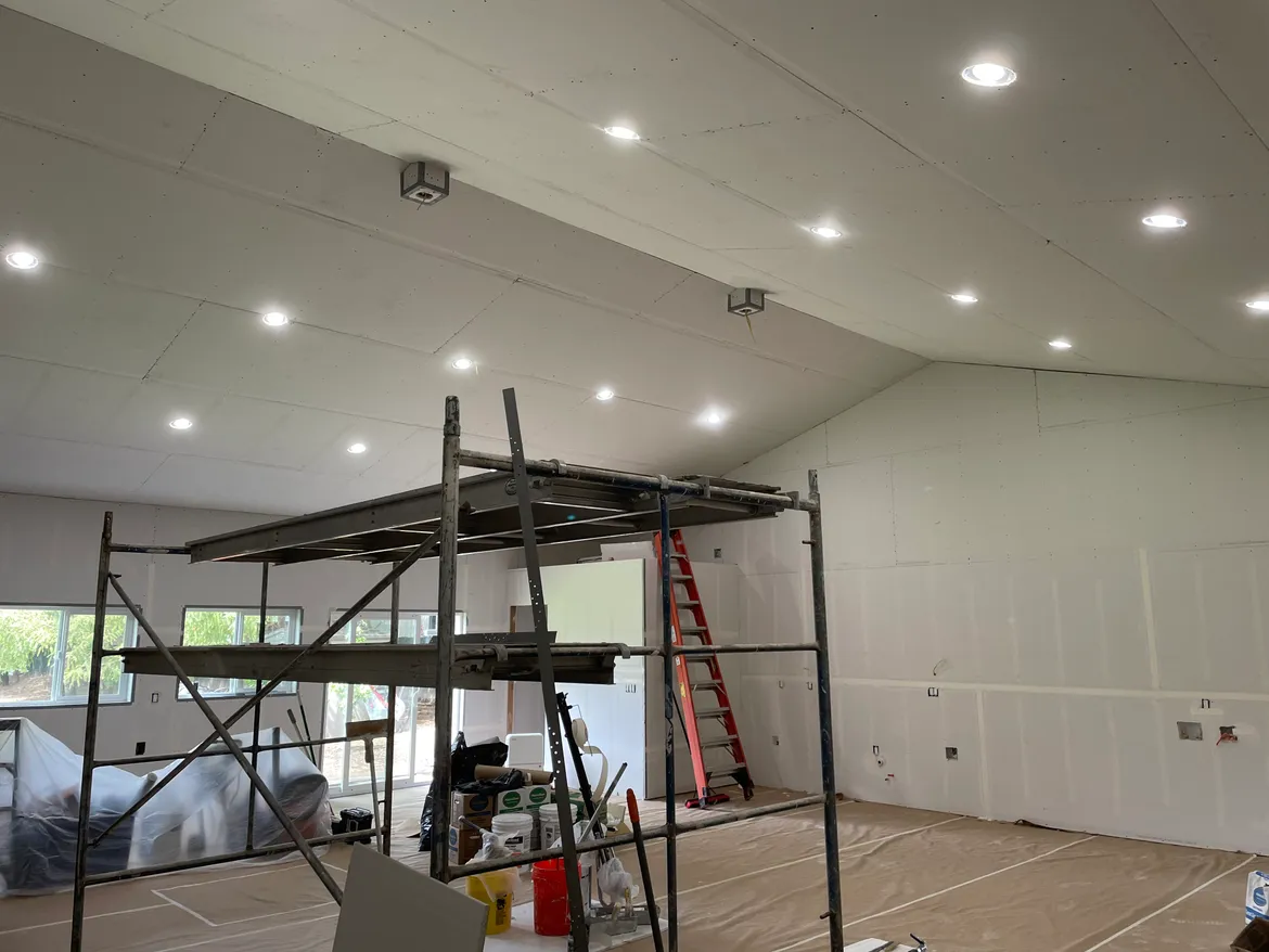 Vaulted ceiling drywall installation with scaffolding and recessed can lights